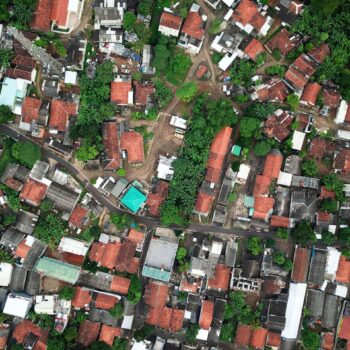 Aerial view of a densely packed neighborhood with red-roofed houses, winding roads, green trees, and various buildings closely situated together.