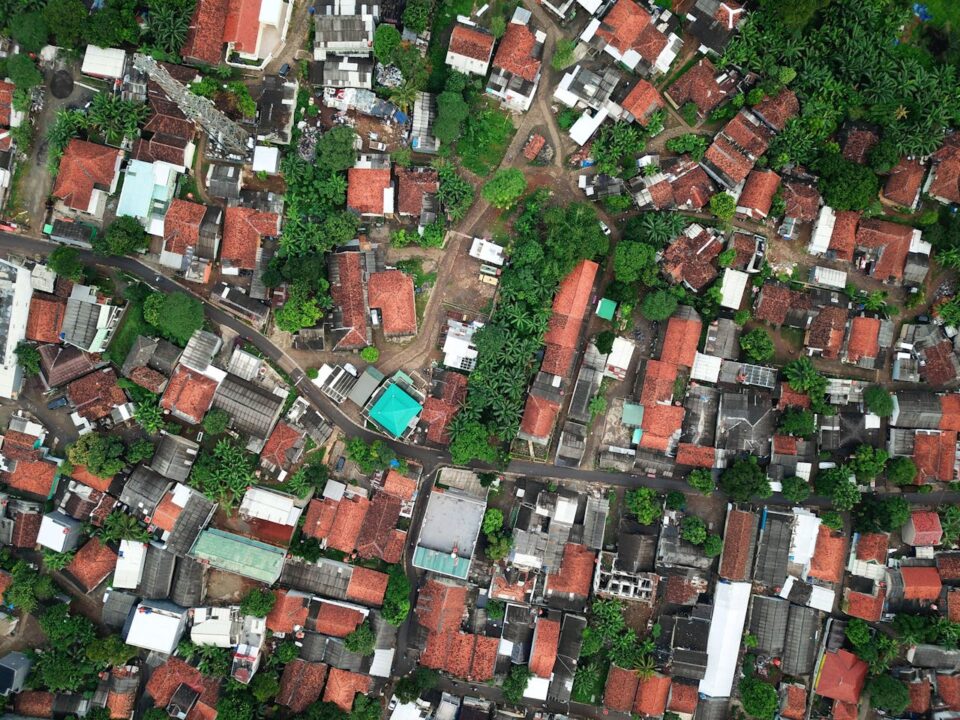 Aerial view of a densely packed neighborhood with red-roofed houses, winding roads, green trees, and various buildings closely situated together.