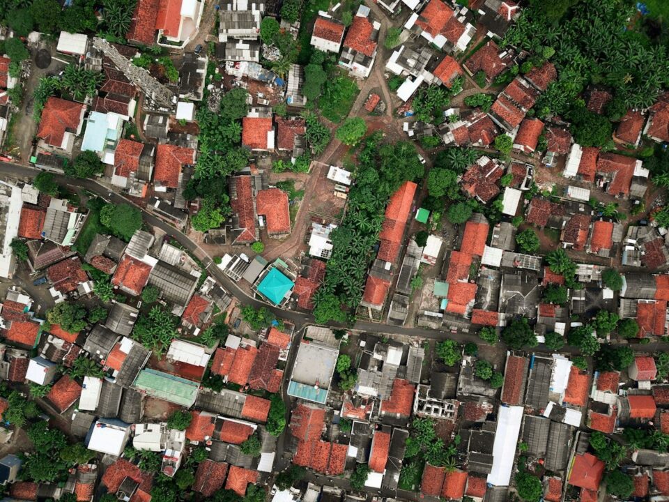 Aerial view of a densely packed neighborhood with red-roofed houses, green trees, and narrow roads winding through the area.